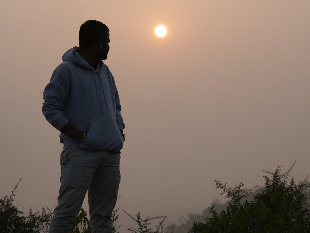 A lone figure silhouetted against the sun through Aravalli haze